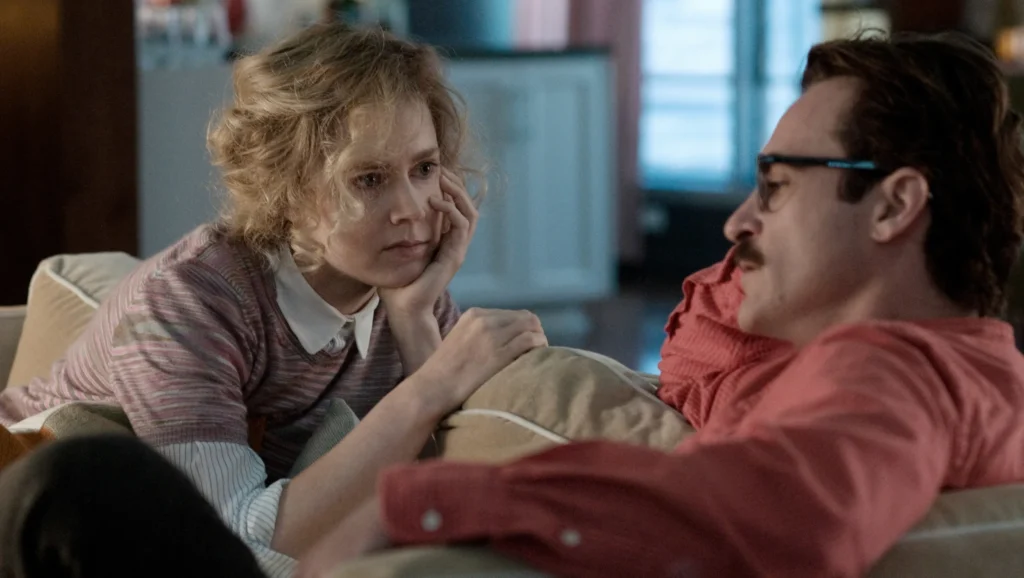 Still from the movie Her, directed by Spike Jonze. Amy Adams and Joaquin Phoenix are shown having a conversation on a sofa.